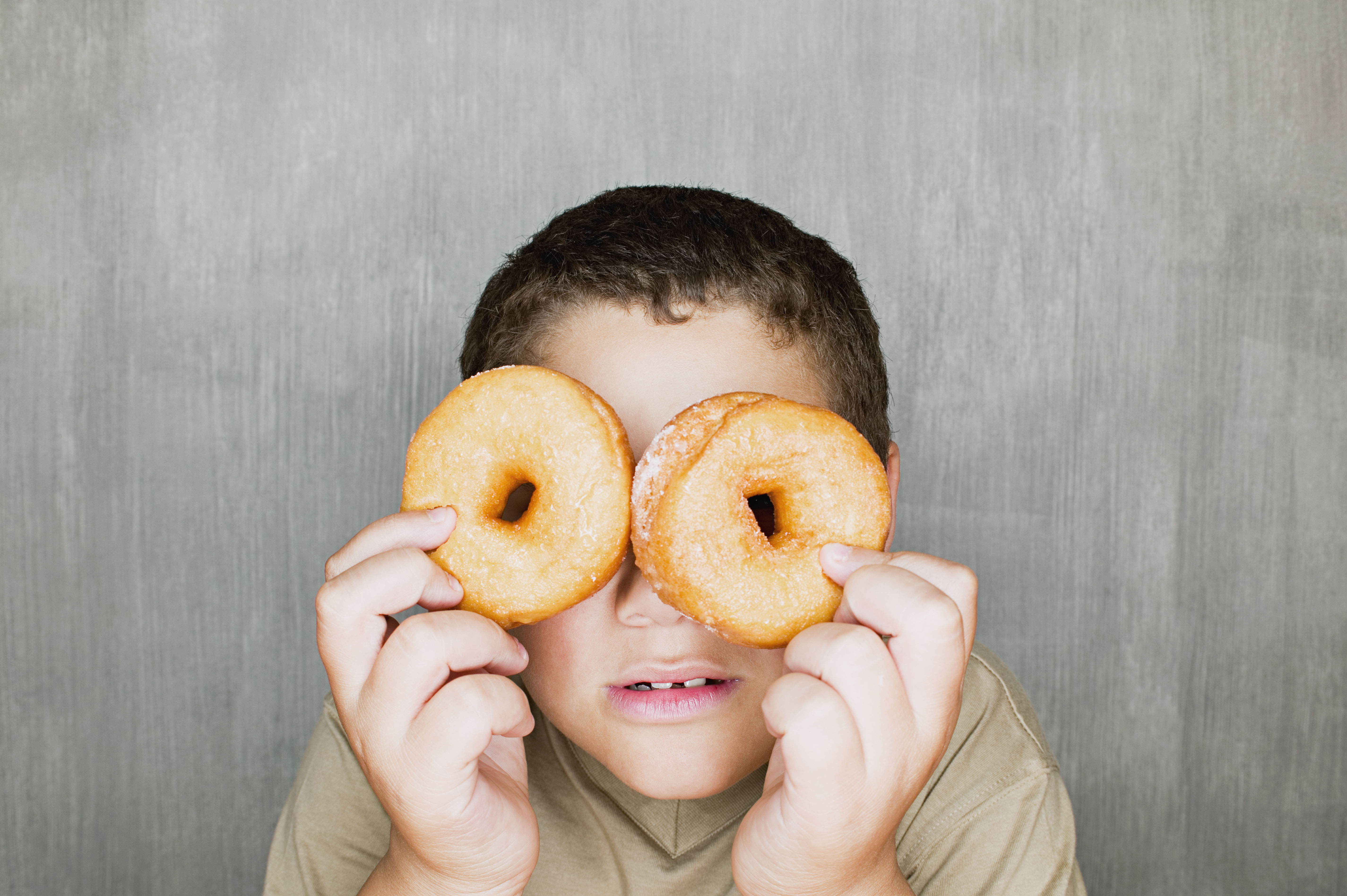 Boy holding doughnuts over eyes