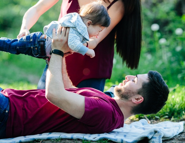 father-lying-in-a-park-with-his-baby-up-and-his-mother-helping-him_1153-2059.png